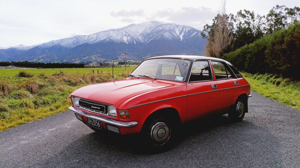 Austin Allegro in New Zealand parked on an empty road at the foot of a snow-capped mountain range